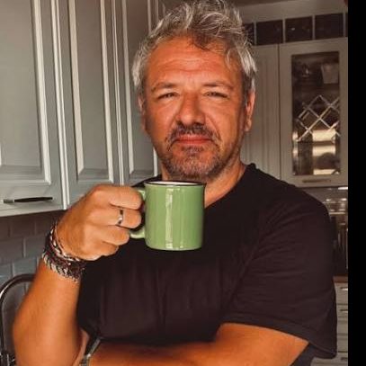 Luca in cucina, maglietta nera, una tazza di caffè verde in mano