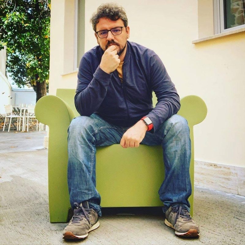 Luca seduto su una poltrona verde in un cortile, la mano al mento