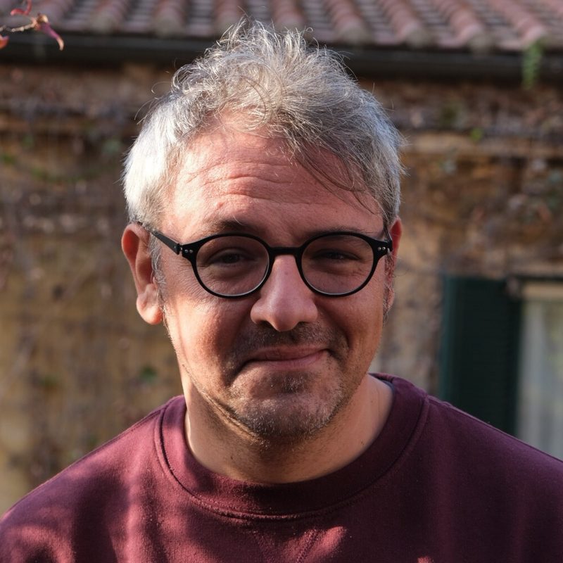 Luca Salici, occhiali tondi e maglia bordeaux, in un cortile a Roma